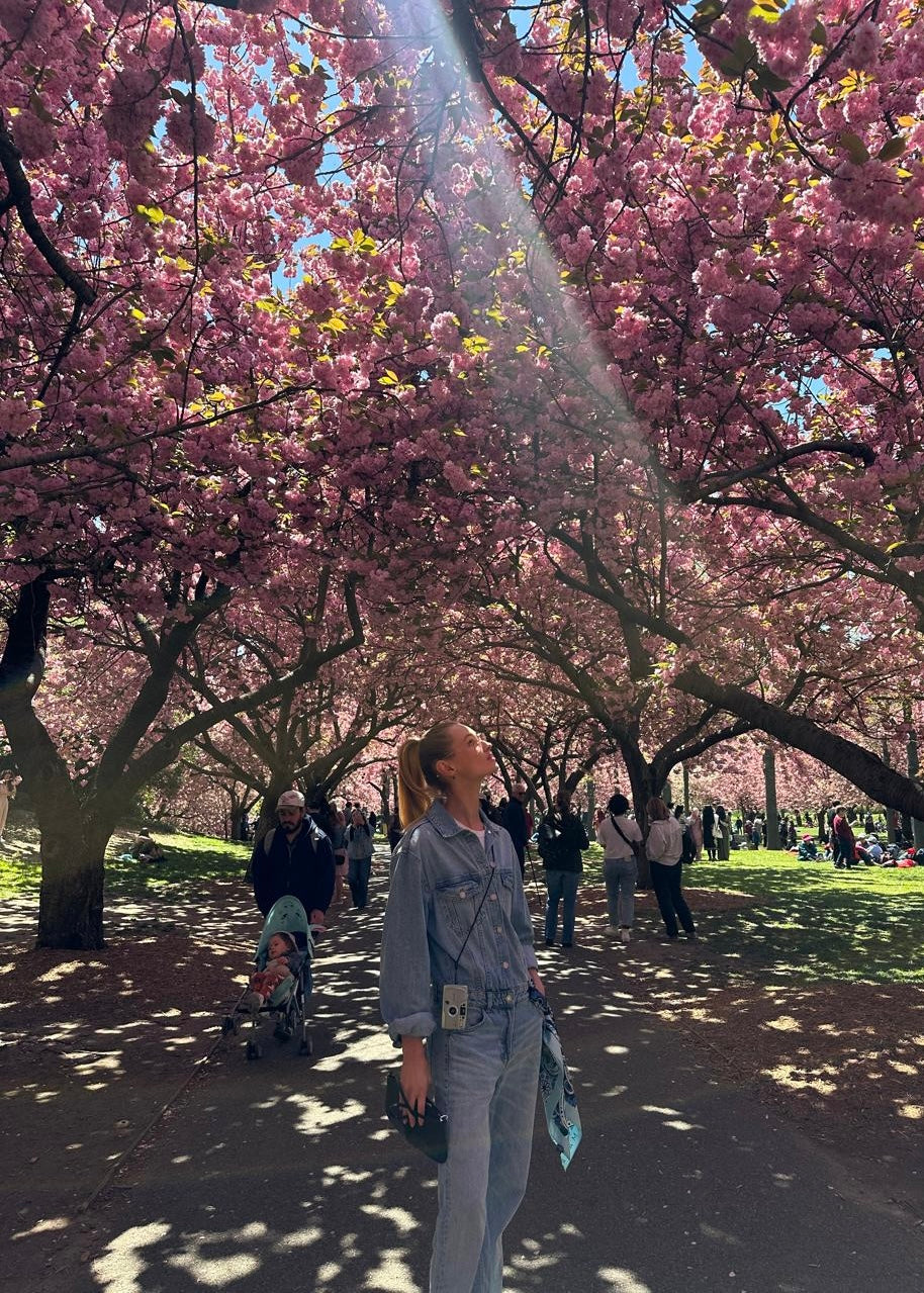 Woman holding the Aurora blue silk scarf at Brooklyn Botanic Garden with cherry blossoms in the background — a vibrant, flowing Italian silk accessory styled with soft elegance in nature.